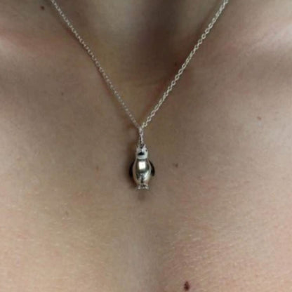 A close-up of a person's neck and chest wearing a delicate silver chain necklace with a small penguin-shaped pendant.