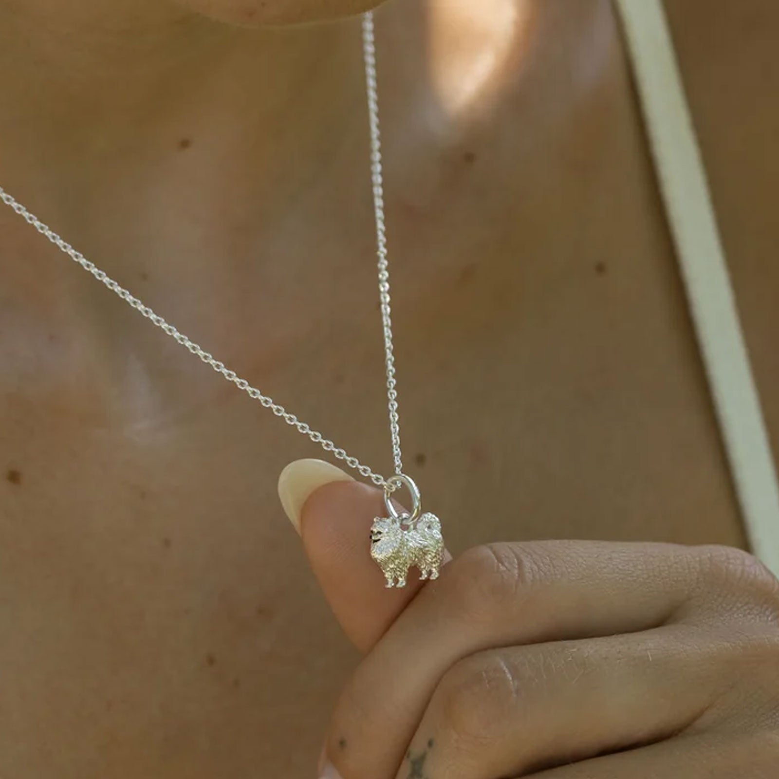 Silver dog necklace with a small pendant held by a hand against a neutral background