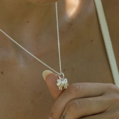 Silver dog necklace with a small pendant held by a hand against a neutral background