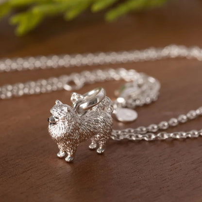 Silver pomeranian dog-shaped pendant on a chain against a wooden background