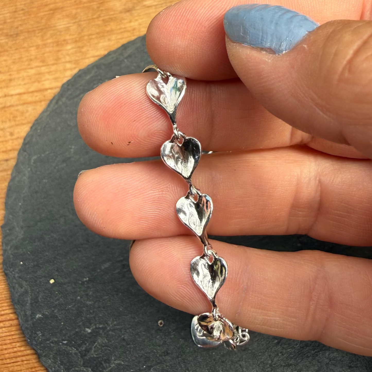Hand holding a silver heart-shaped bracelet on a wooden surface