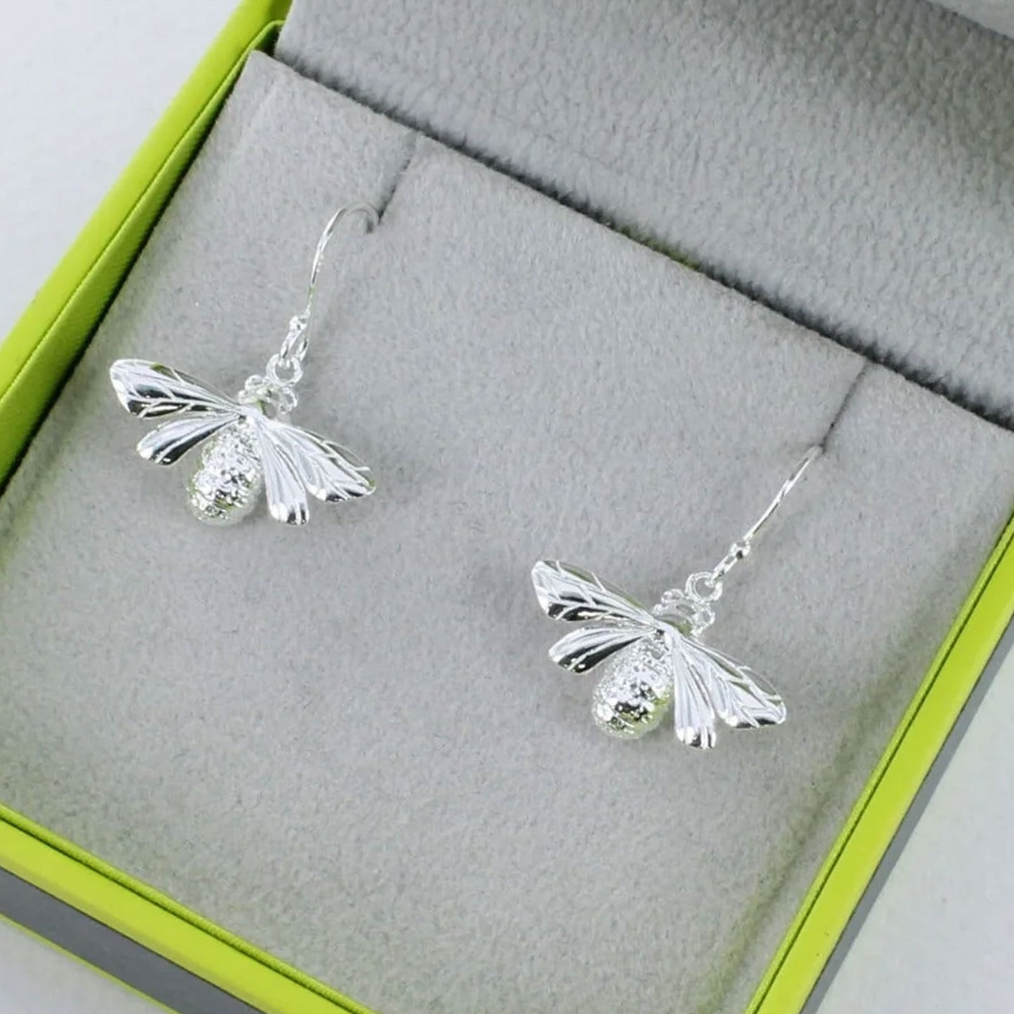 Silver bee earrings on a grey jewelry box with green trim
