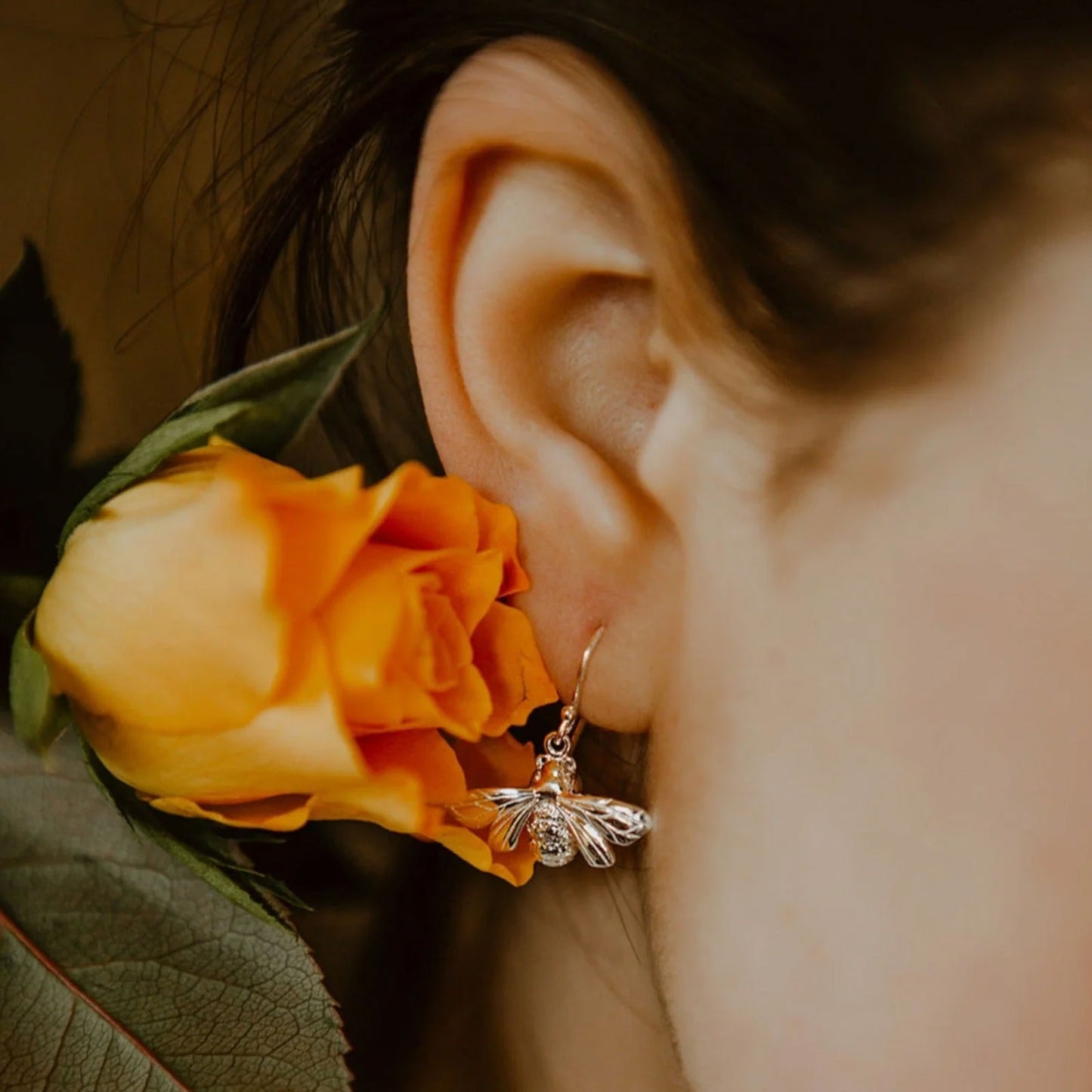 Close-up of an ear with a decorative bee earring and orange flower.