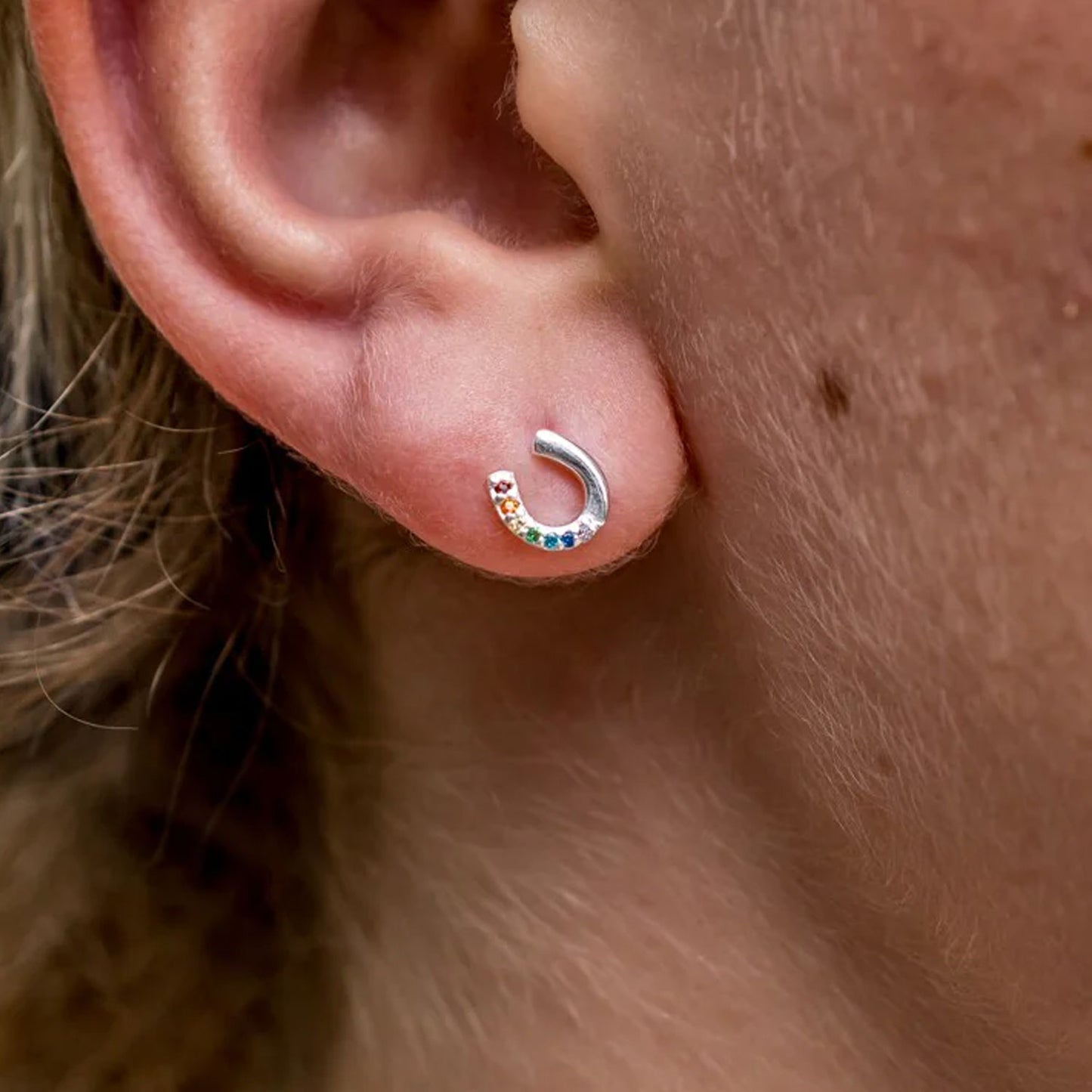 Close-up of a silver earring with colorful stones on an ear.