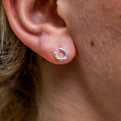 Close-up of a silver earring with colorful stones on an ear.