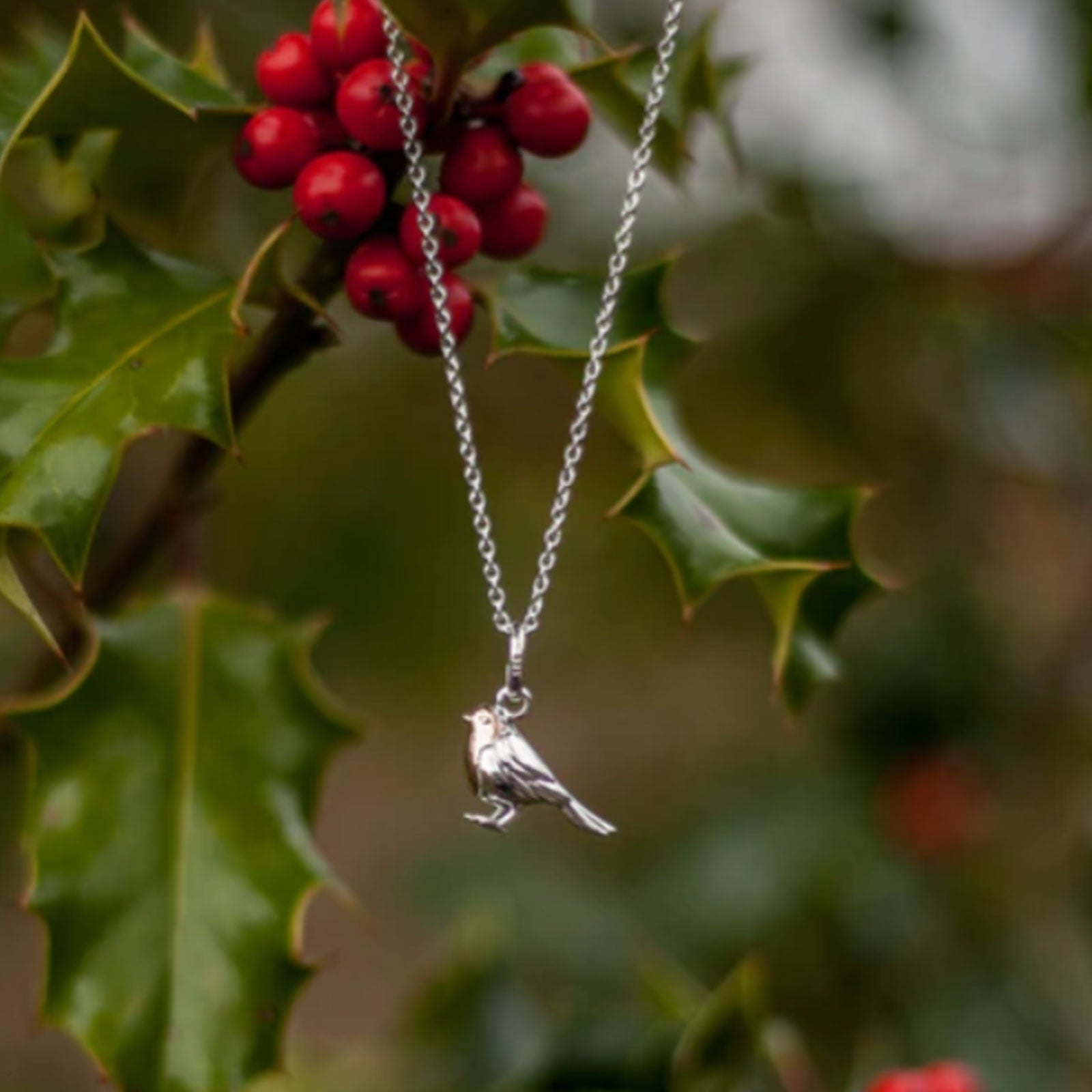 Silver bird necklace hanging among red berries and green leaves