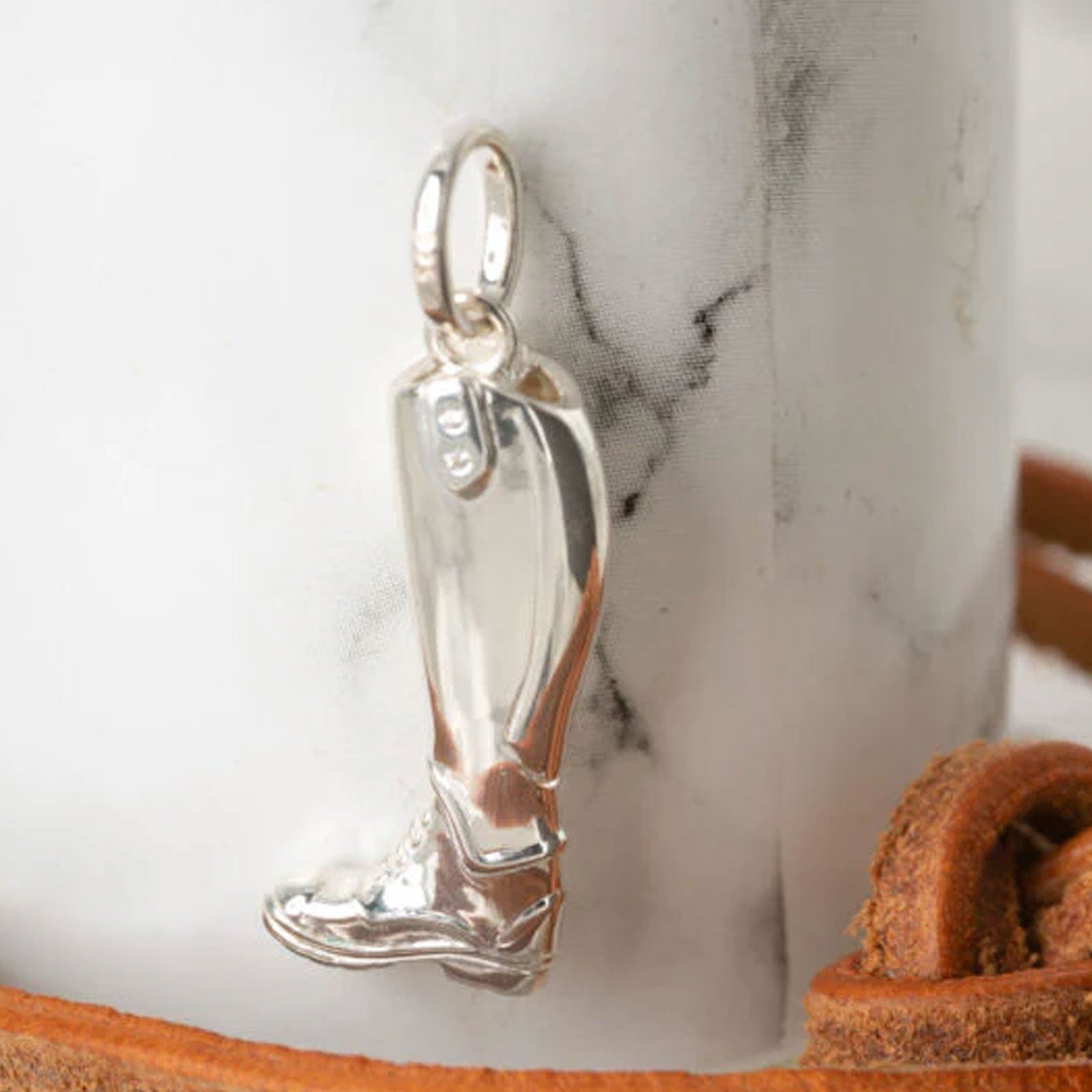 Silver riding boot charm on a marble surface