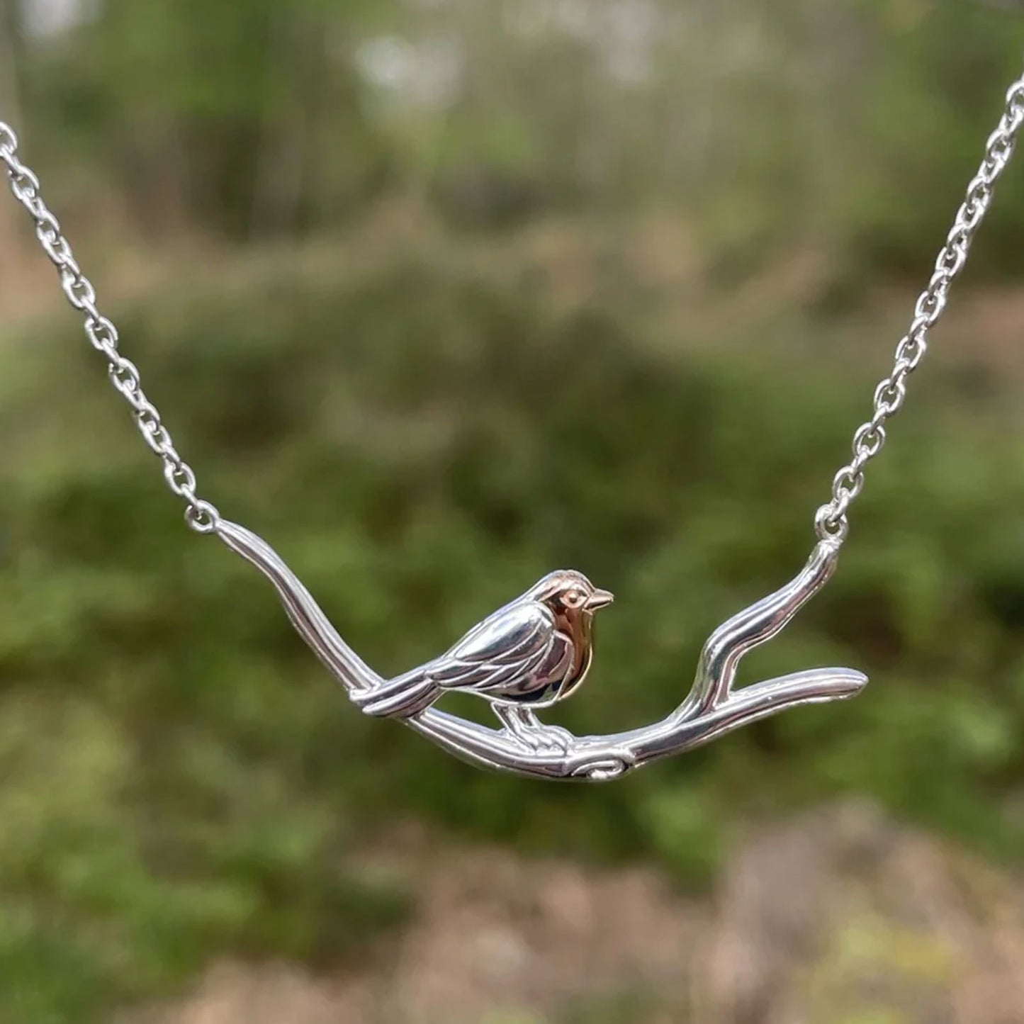 Silver bird necklace on a branch with a blurred green background