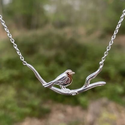 Silver bird necklace on a branch with a blurred green background