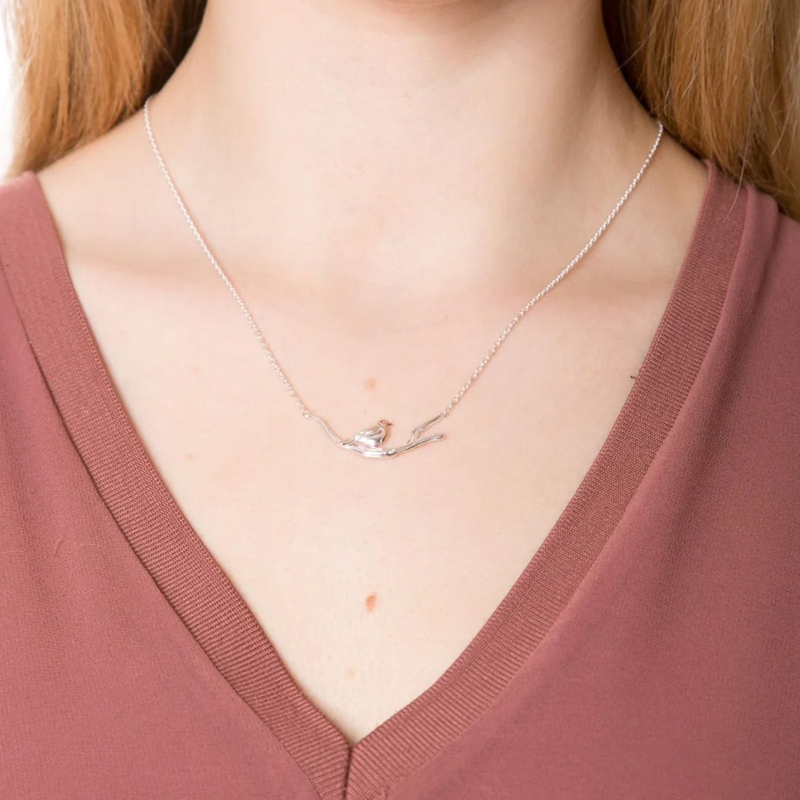 Necklace with a bird pendant worn by a person in a pink shirt