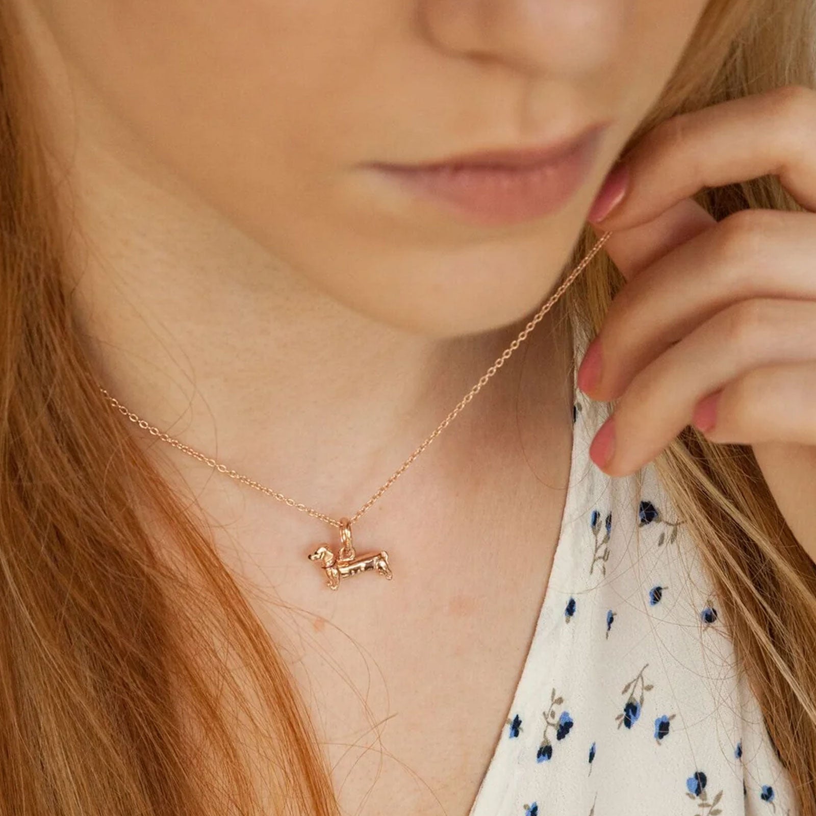 Rose gold dog-shaped pendant necklace worn by a person with long hair.