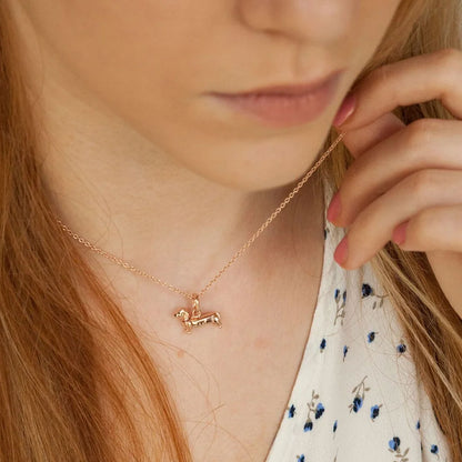 Rose gold dog-shaped pendant necklace worn by a person with long hair.
