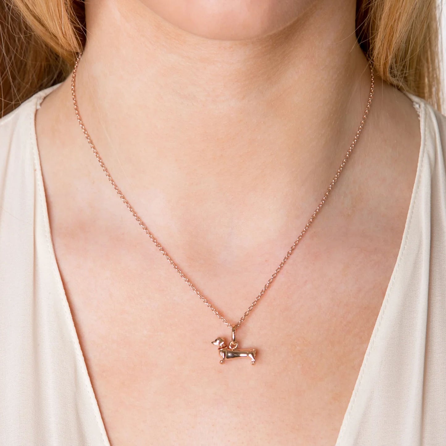 Rose gold necklace with a small dog pendant on a person wearing a white top.