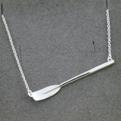 A silver-toned necklace featuring a polished rowing blade on a delicate link chain, displayed against a dark grey textured background.