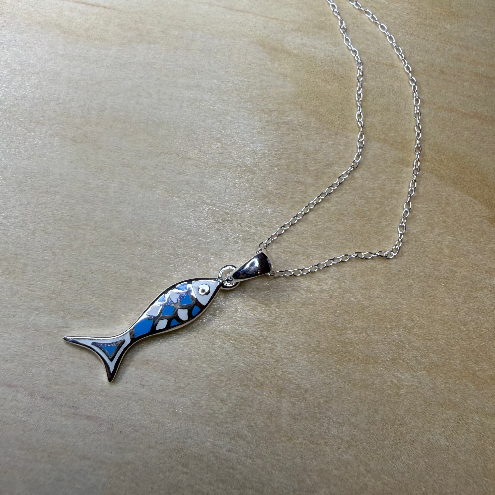Fish-shaped pendant on a chain against a beige background