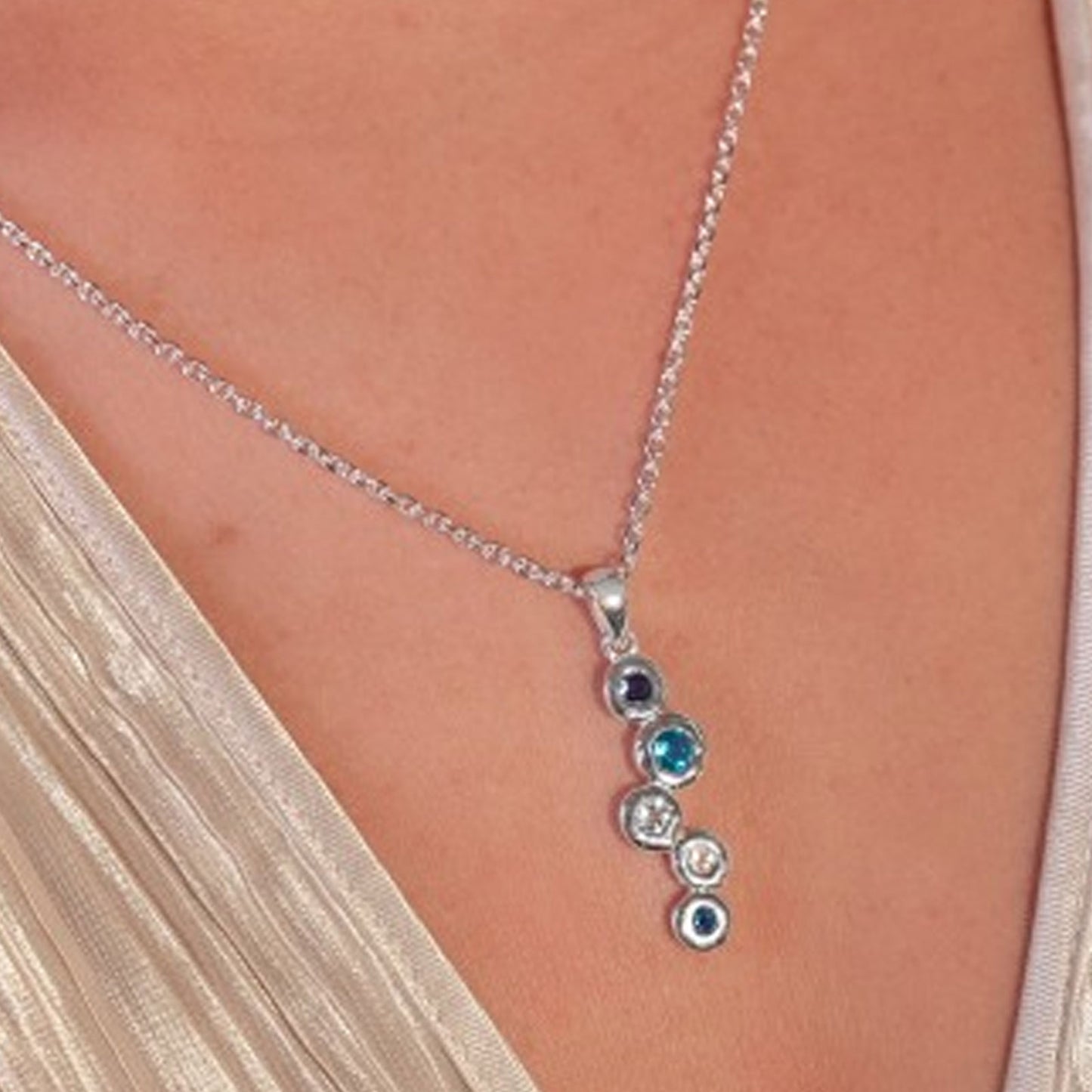 Necklace with circular pendant featuring blue and clear stones on a person wearing a beige top.