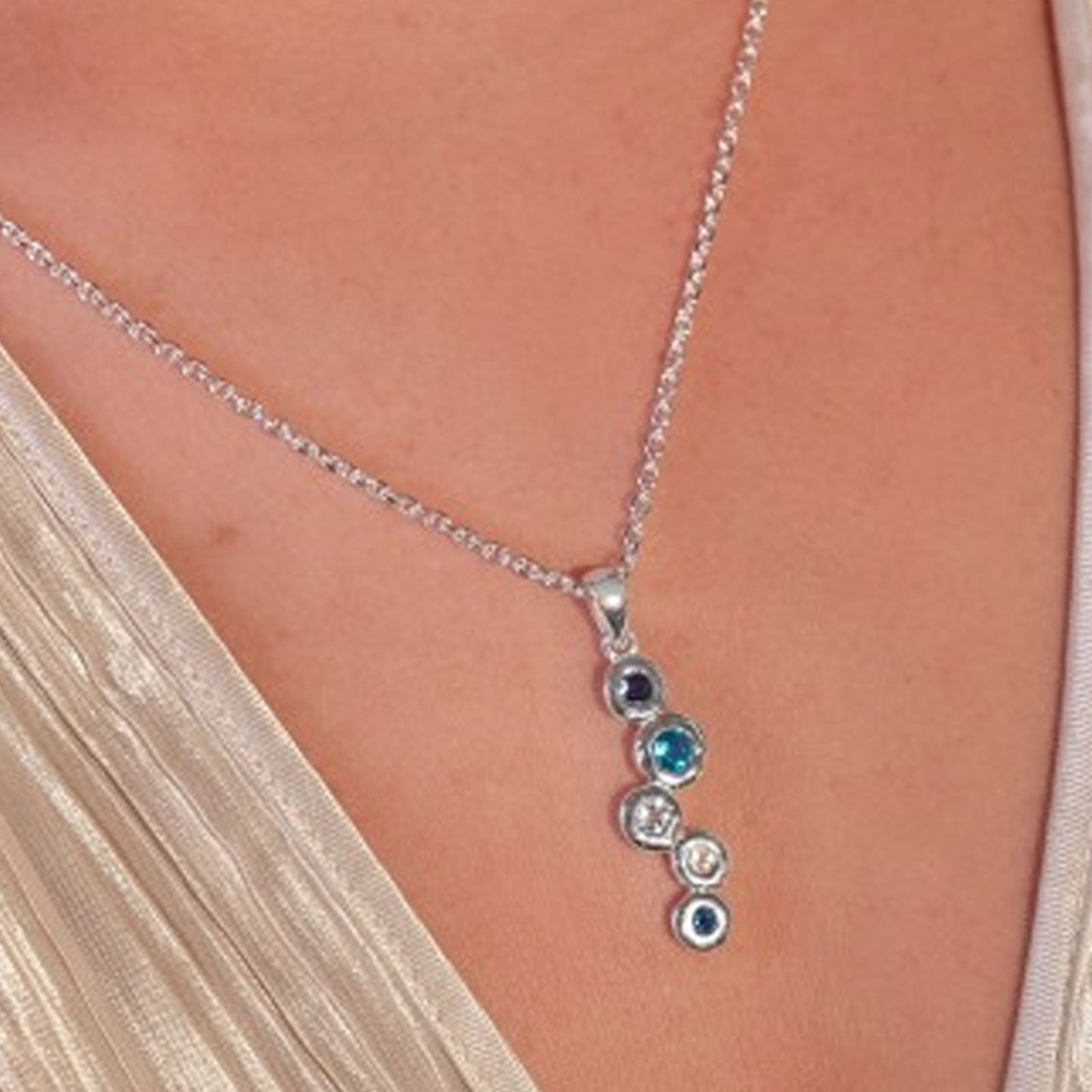 Necklace with circular pendant featuring blue and clear stones on a person wearing a beige top.