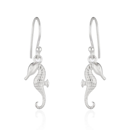 A pair of silver seahorse drop earrings with textured bodies and curved hook backs, shown on a clean white background with a soft reflection below.