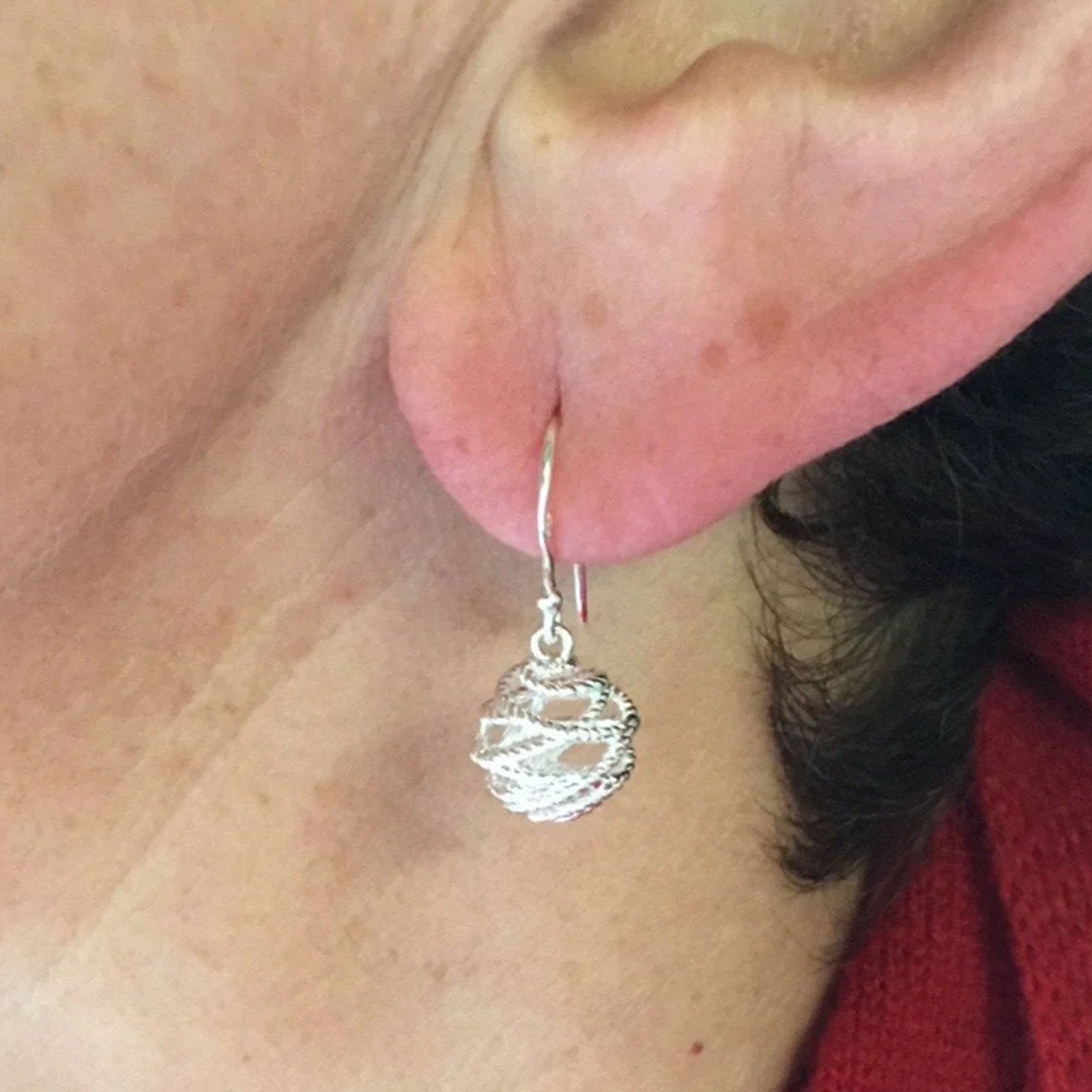 Close-up of a silver earring worn by a person with a red garment in the background