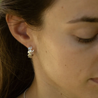 A close-up of a woman's ear wearing a small  leaf-shaped stud earring.