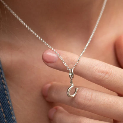 Silver necklace with a horseshoe pendant held by a hand