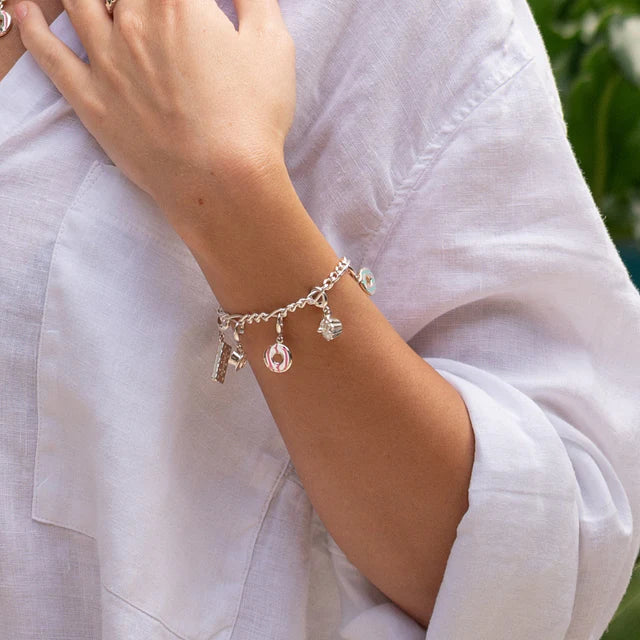 Silver bracelet with charms on a wrist against a white shirt background