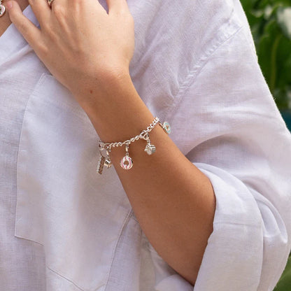 Silver bracelet with charms on a wrist against a white shirt background