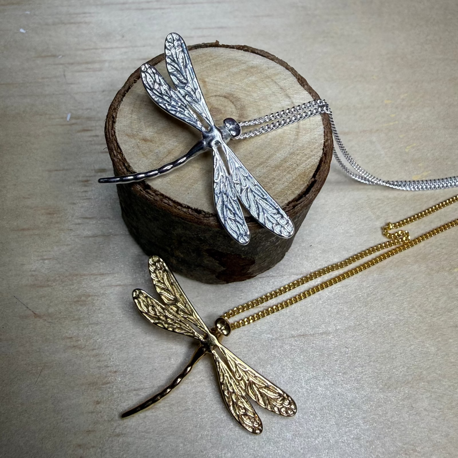 Two dragonfly-shaped pendants on wooden and metal stands.