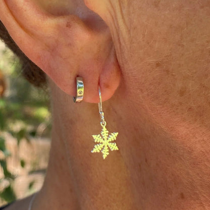 A close-up of a person's ear wearing a small silver hoop earring with a dangling gold snowflake charm.