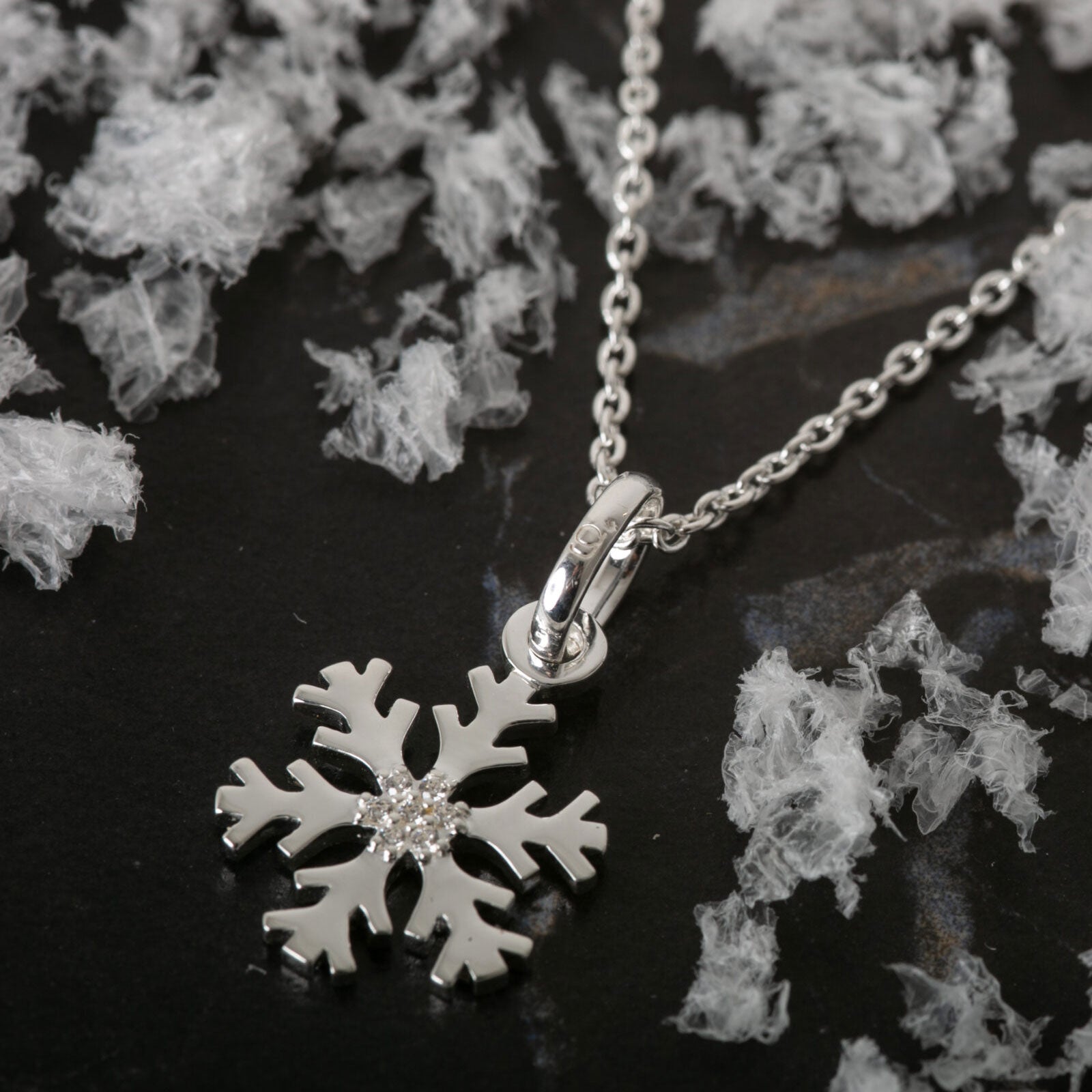 Silver snowflake pendant necklace on a dark surface with decorative elements