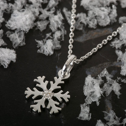 Silver snowflake pendant necklace on a dark surface with decorative elements
