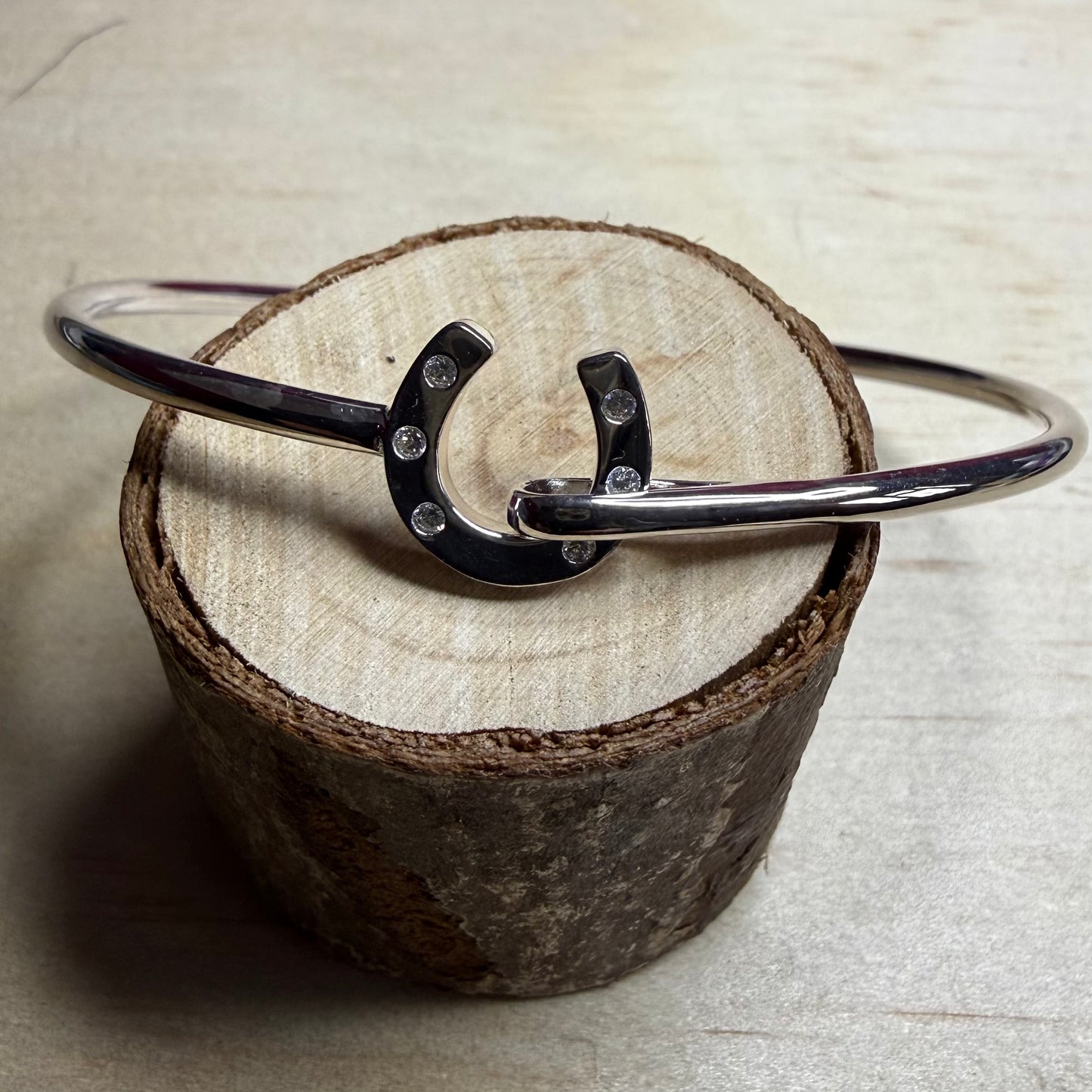 Silver bracelet with a horseshoe charm on a wooden block