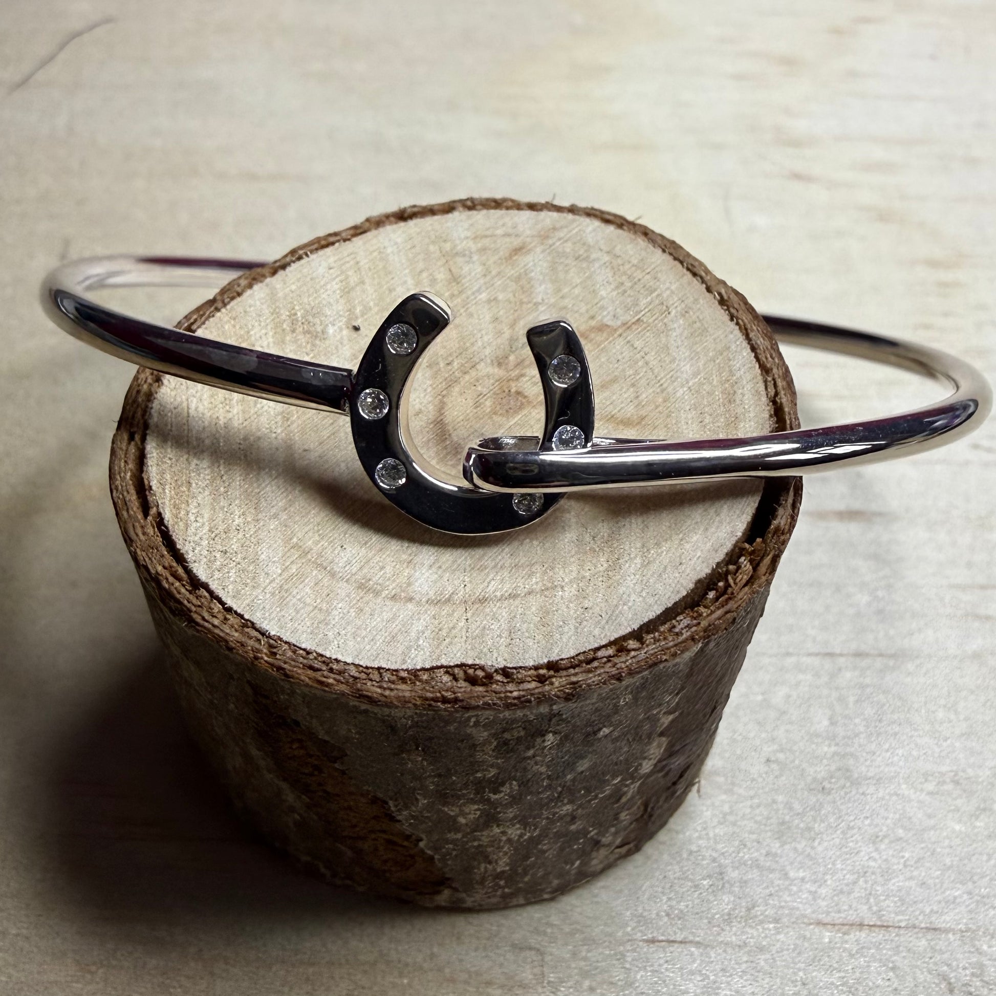 Silver bracelet with a horseshoe charm on a wooden block