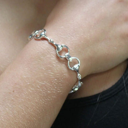 A close-up of a silver horsebit chain bracelet worn on a person's wrist, with skin and a black shirt visible in the frame.