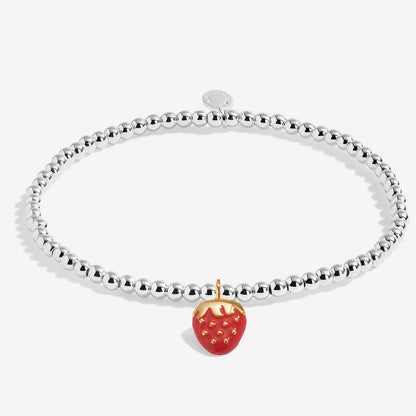 A silver beaded bracelet with a dangling strawberry charm featuring red enamel and gold details, shown on a light gray background.