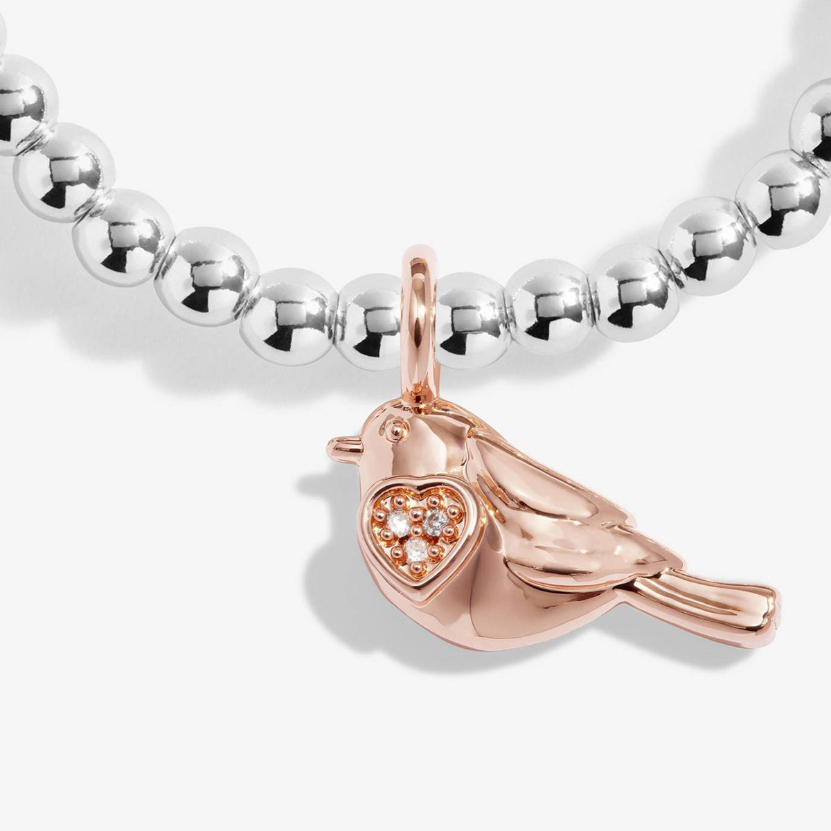 A close-up of a beaded necklace with polished silver round beads and a rose gold bird pendant featuring a heart-shaped crystal cluster, on a light gray background.