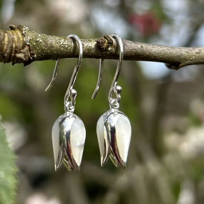Silver tulip-shaped earrings hanging from a branch with a natural background