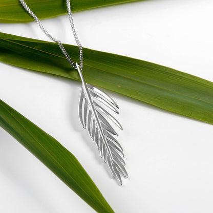 Silver feather-shaped pendant on a chain with green leaves in the background