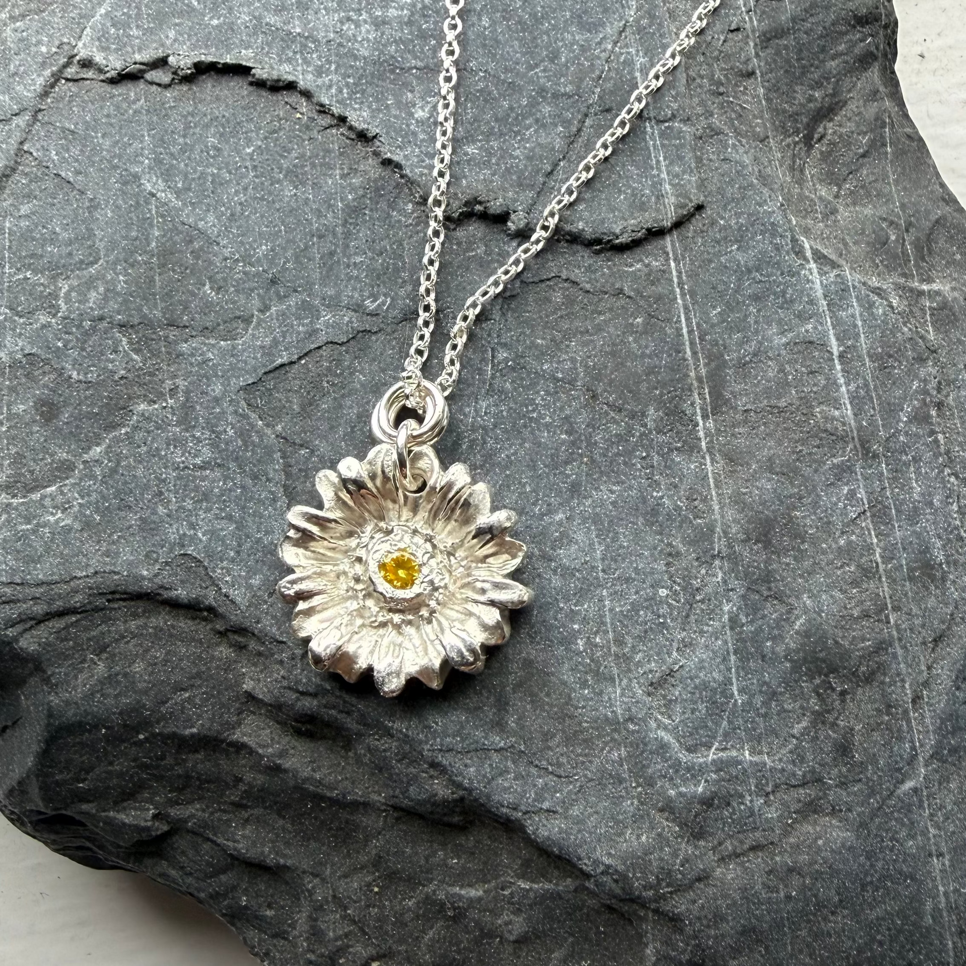 Silver necklace with a flower pendant on a gray stone surface